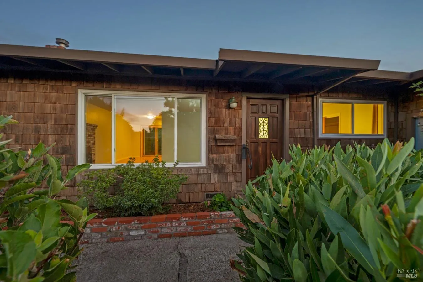 Twilight entry of 4772 Sunshine Avenue with wood-shingle siding and warm interior light