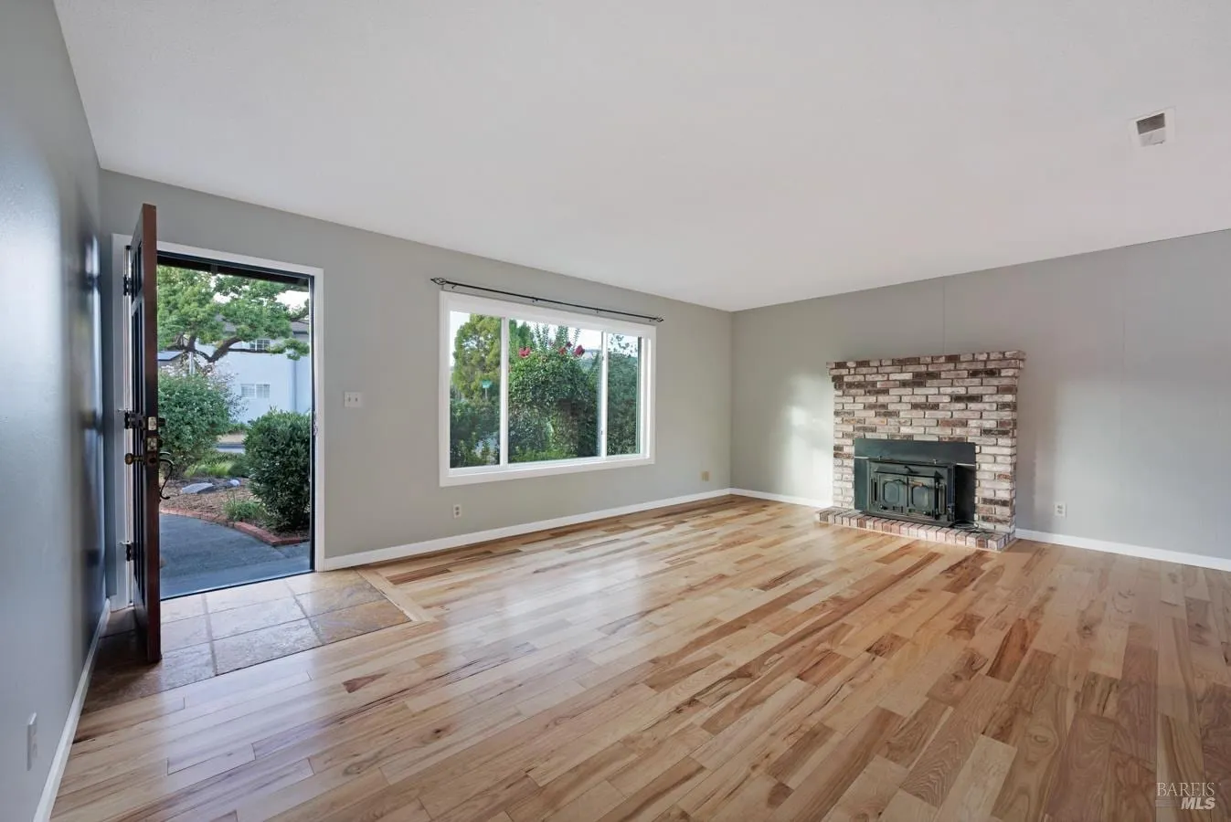 Living room with brick fireplace, hardwood floors, and front entry